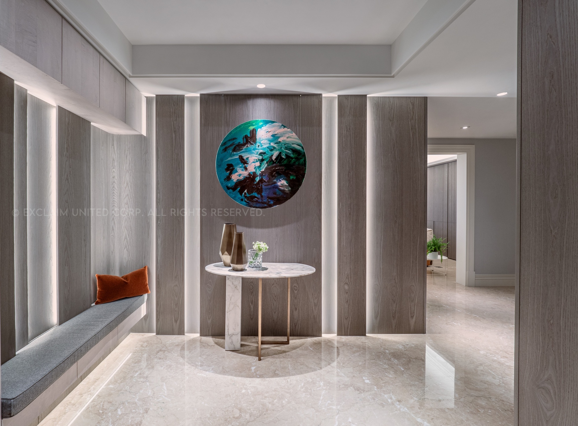 首先，將入室後的玄關區，作為家的起始點，透過具層次感的藝術手法，卸除原玄關二進的雙開電動門，調整為收納機能的衣帽間，有條不紊地歸納與收整屋主一家人喜愛的露營用品、鞋類與登山用具。視覺設計上，具有氣派豪宅的感受，並揉合大地色系的木紋肌理為立面，層層疊疊的視覺技法，呼應山林間的自然韻律，將大自然的山嵐曙光意象，轉化為中央圓形藝術畫作之端景，伴隨兩側與穿鞋椅區輕灑的接光源，彷彿將戶外露營、登山時，欣賞到林間綠意的動人景緻，移植入室，構築深刻的時序意境。